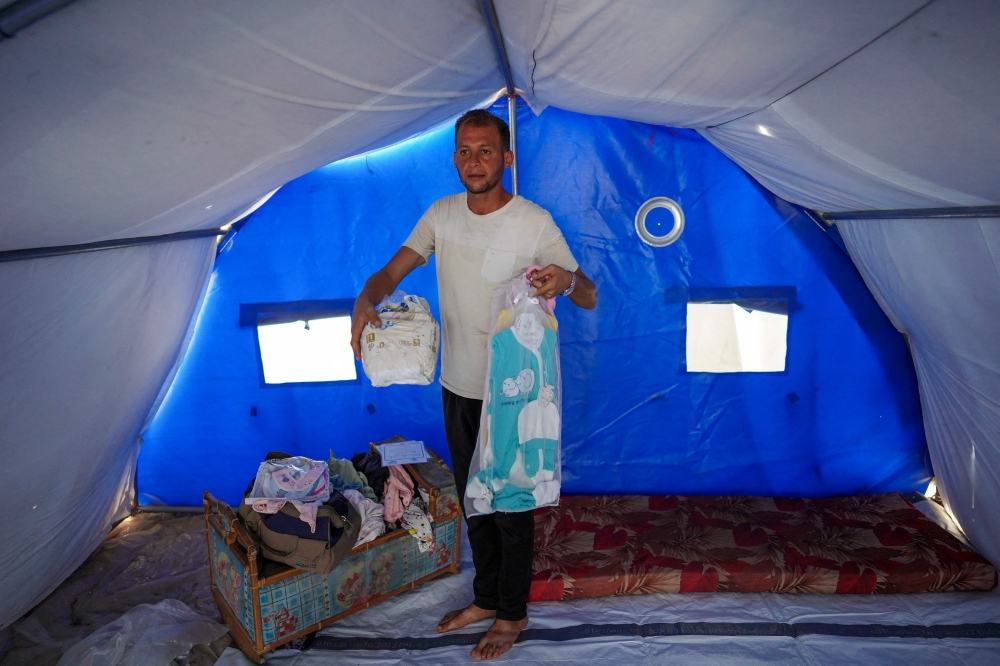 Mohammed Abu al-Qumsan shows clothes of his twin children, who were killed during Israeli bombardmen in central Gaza on August 10, 2024, as he stands in his tent at a camp for displaced Palestinians in Khan Yunis, in the southern Gaza Strip on August 15, 2024, amid the ongoing conflict between Israel and the Hamas group. — AFP pic