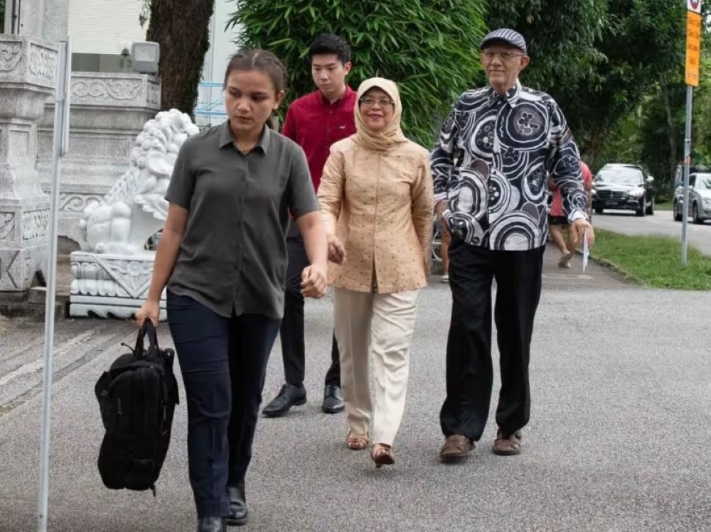 Lim Hwee Yi (left) leads the way ahead of then Singapore president Halimah Yacob and her husband Mohammed Abdullah Alhabshee outside a polling station at Chung Cheng High School (Main) on September 1, 2023 for the Singapore presidential elections. — Picture via TODAY