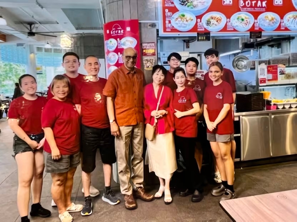 Singapore president Tharman Shanmugaratnam (5th from left) and his wife Jane Ittogi (6th from left) visiting Lim Hwee Yi’s porridge stall in July 2024. — Picture via TODAY