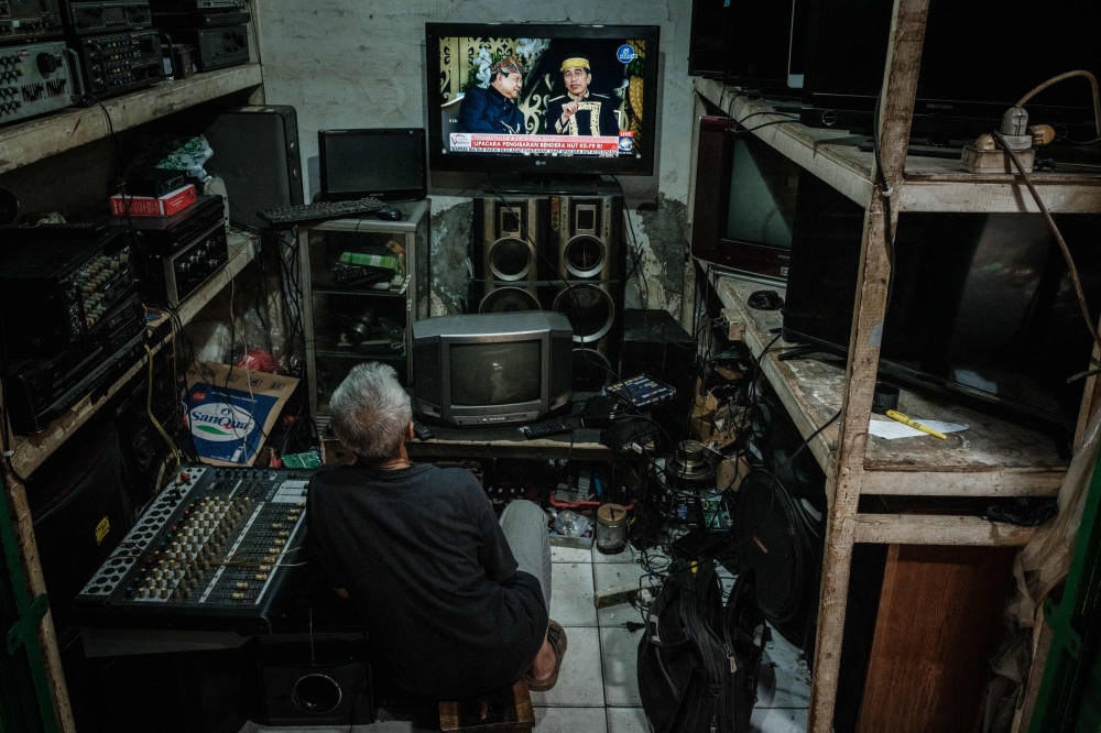 A man watches television screen showing Indonesia's President Joko Widodo (right) and Indonesia's Defence Minister and President-elect Prabowo Subianto during a live broadcast of Indonesia's 79th Independence Day celebrations from the future presidential palace in the future capital Nusantara, at his electrical recycling workshop in Jakarta on August 17, 2024. — AFP pic