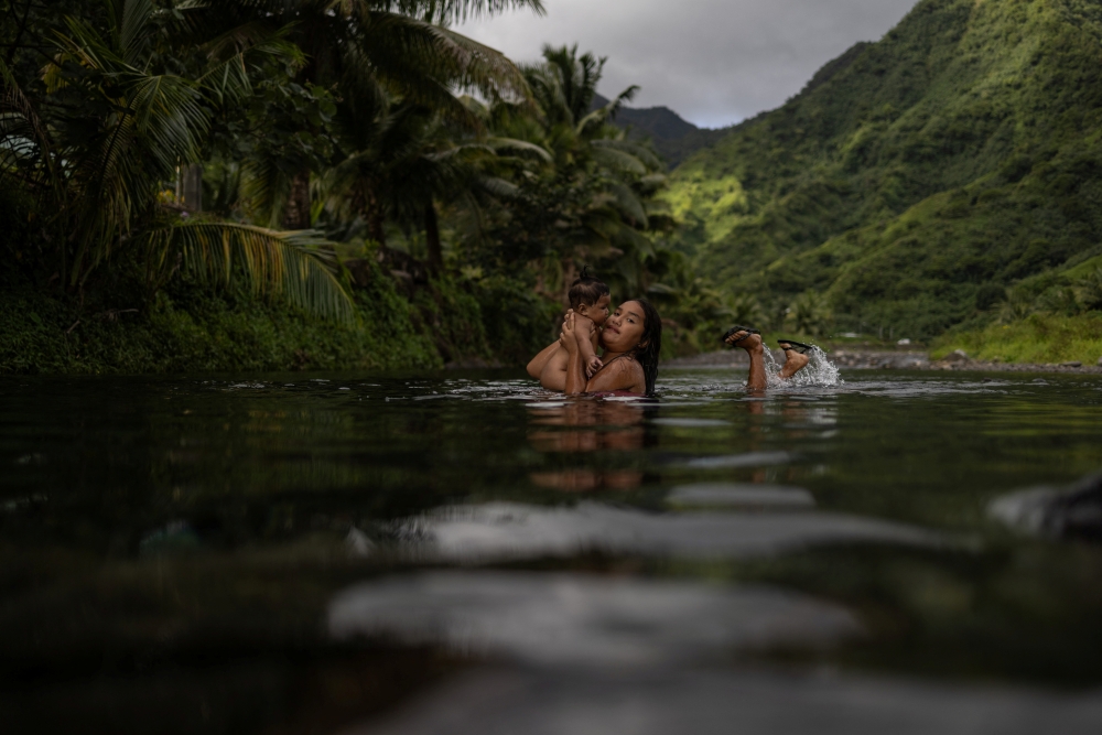 Uratua holds six-month-old Kiana as they play inside a freshwater stream in Teahupo'o, Tahiti, French Polynesia, August 3, 2024. — Reuters pic