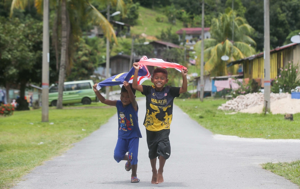 Children from the Kampung Orang Asli Chadak, Ulu Kinta in Perak running with the  national flag ‘Jalur Gemilang’ in this file picture. — Picture by Farhan Najib