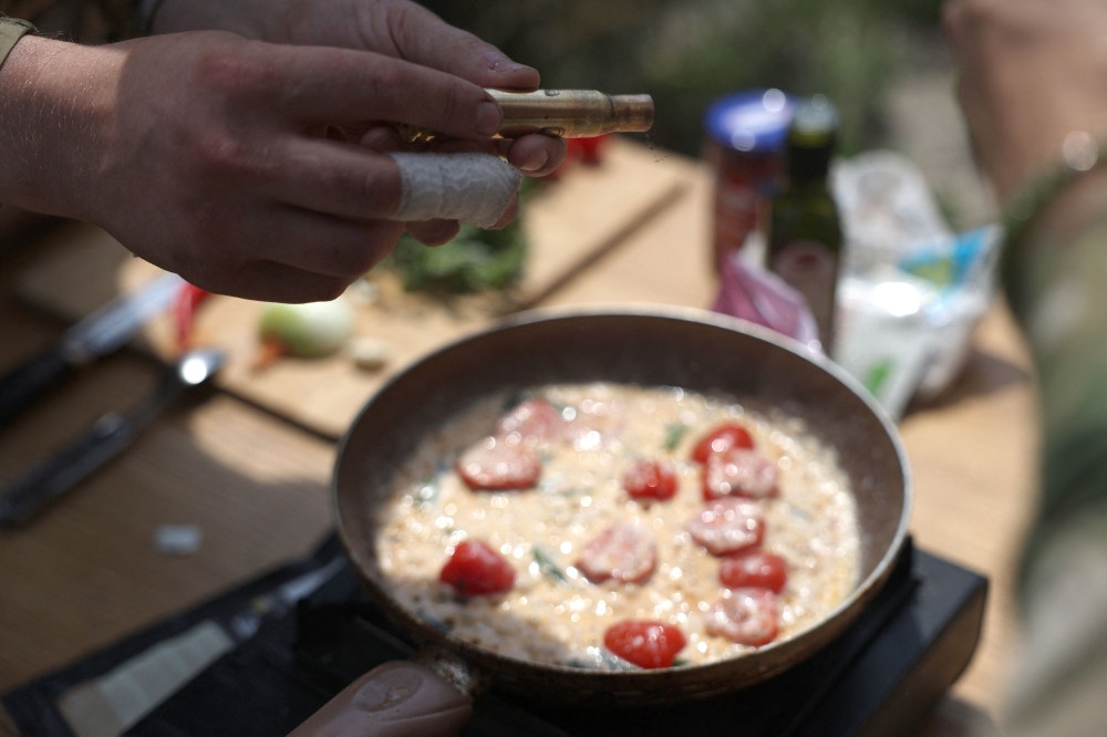 Ukrainian serviceman and influencer Ruslan Mokrytskyi shows a bullet casing containing spices while cooking pasta during video recording for Tik Tok in an undisclosed location in the Donetsk region July 27, 2024. — AFP pic