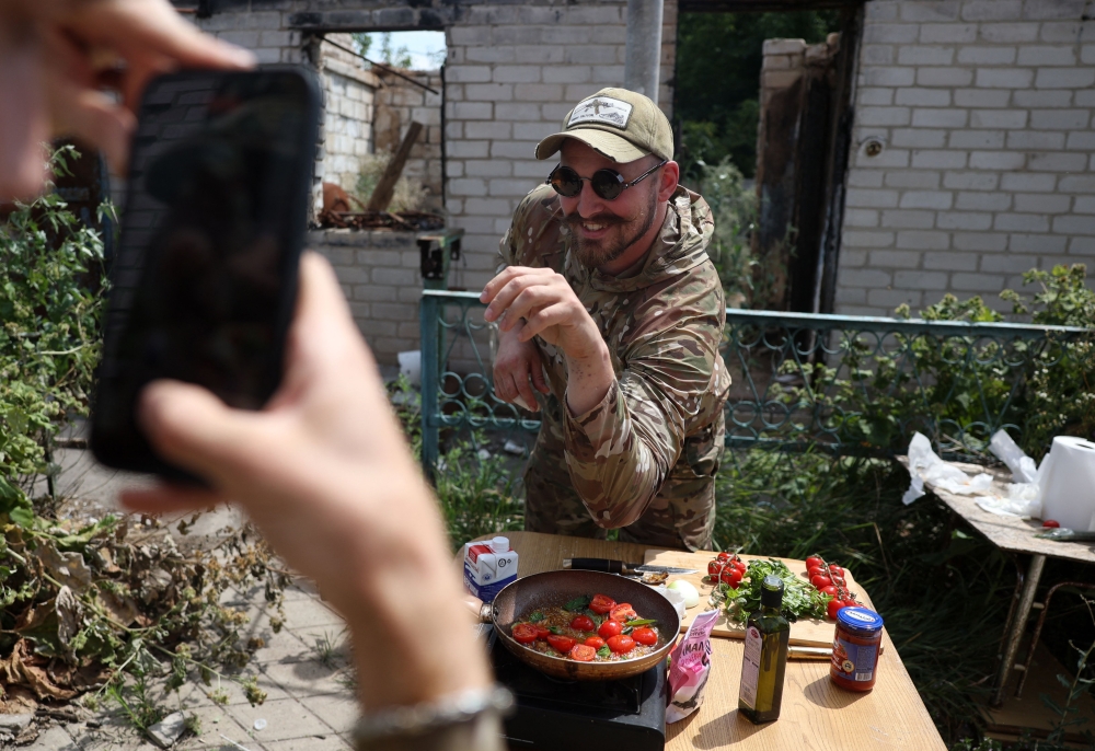 Ukrainian serviceman and influencer Ruslan Mokrytskyi poses for the camera as he cooks pasta as his fellow soldier records a video of him for Tik Tok in an undisclosed location in the Donetsk region, on July 27, 2024, amid the Russian invasion in Ukraine. — AFP pic