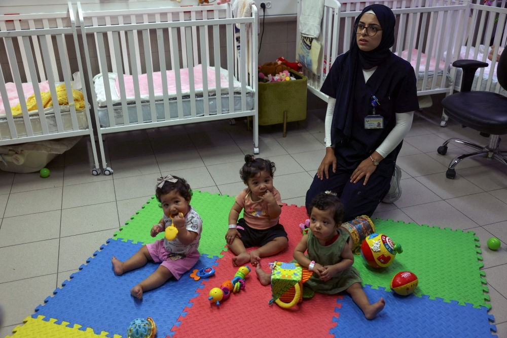 A nurse watches over as Palestinian triplets of Gaza-native Hanane Bayouk, Najmeh (left), Najoua (centre) and Noor, play at the children’s ward of the Al-Maqased Hospital in east Jerusalem July 31, 2024. The triplets were born at the Al-Maqased Hospital where the mother came from the Gaza Strip to give birth, returning soon after when her travel permit issued by Israel expired, leaving her babies in their care. — AFP pic