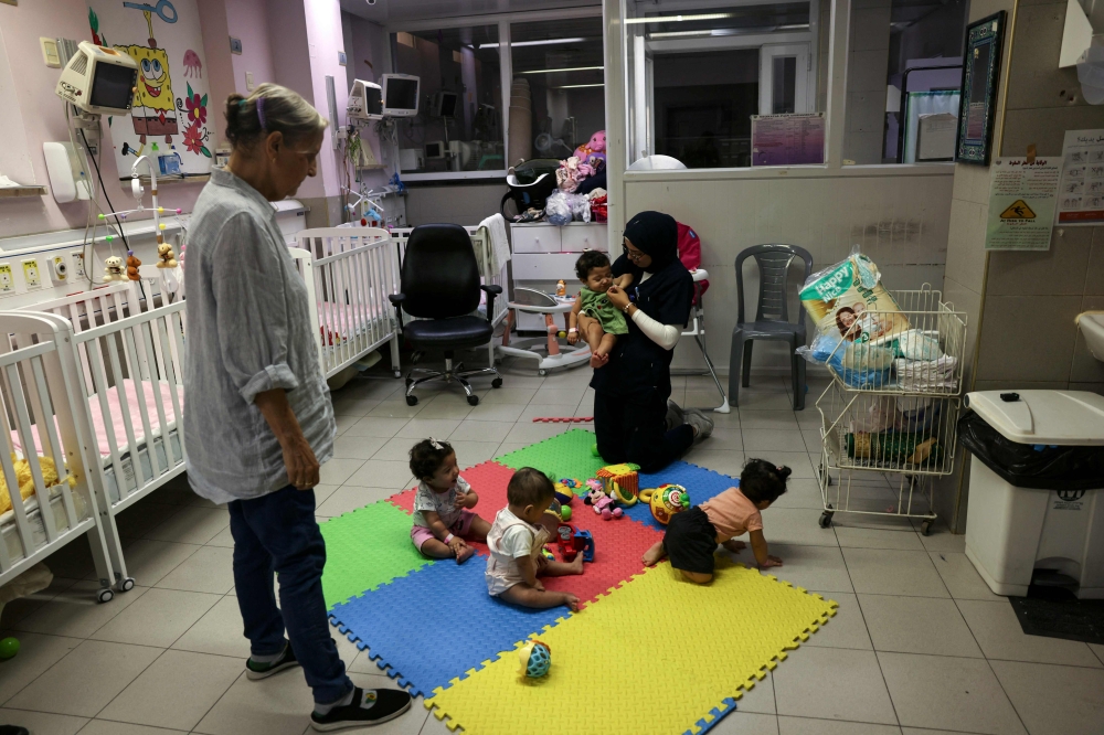  Nurses entertain Palestinian triplets Najmeh (left), Najoua (right) and Noor (held by nurse) of Gaza-native Hanane Bayouk, at the children’s ward of the Al-Maqased Hospital in east Jerusalem July 31, 2024. — AFP pic