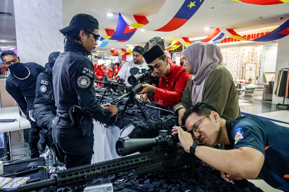 Visitors taking pictures with semi-automatic and automatic weapons at the Mindef booth during the 2024 Umno General Assembly at the World Trade Centre Kuala Lumpur August 23, 2024. — Picture by Firdaus Latif