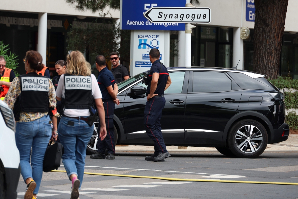 French judicial police officers walk past firefighters following a fire and explosion of cars at a synagogue in La Grande-Motte, south of France, on August 24, 2024. — AFP pic