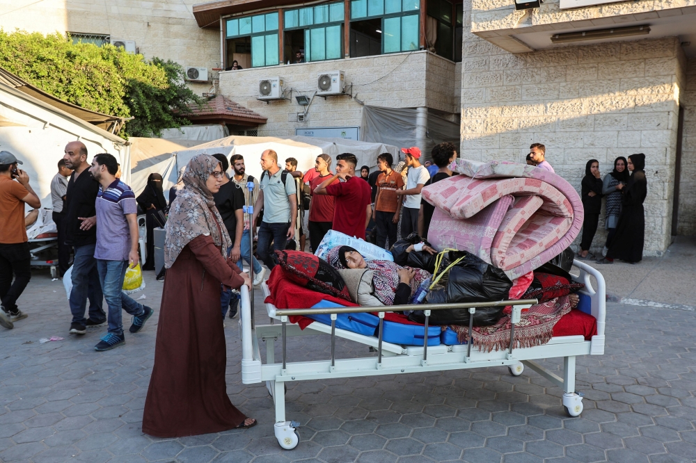 Palestinian patients fearing an Israeli ground operation are assisted to flee Al-Aqsa Martyrs hospital, after Israeli army ordered an evacuation of nearby areas. — AFP pic