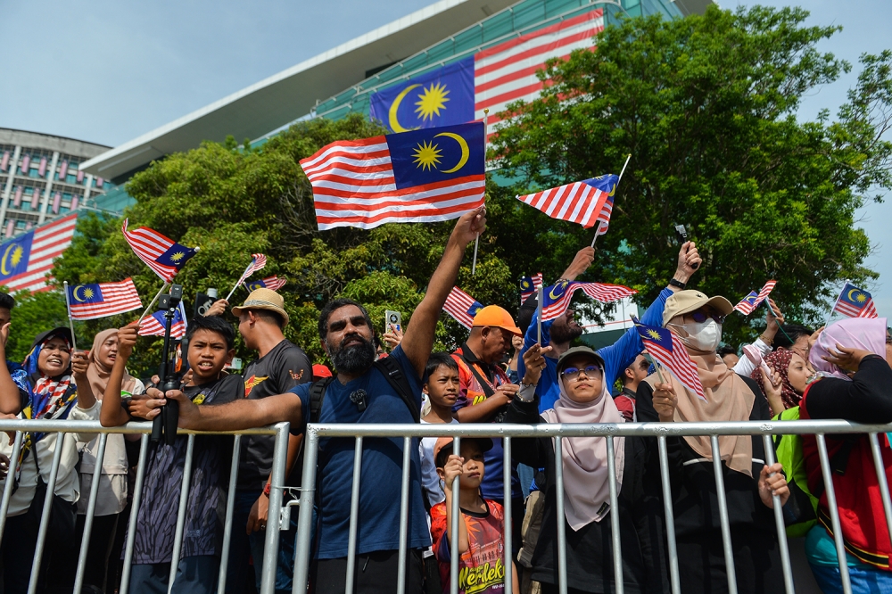 Attendees wave Malaysian flags, also known as Jalur Gemilang, as they watch a parade during National Day celebrations in Putrajaya on August 31, 2023. — Picture by Miera Zulyana