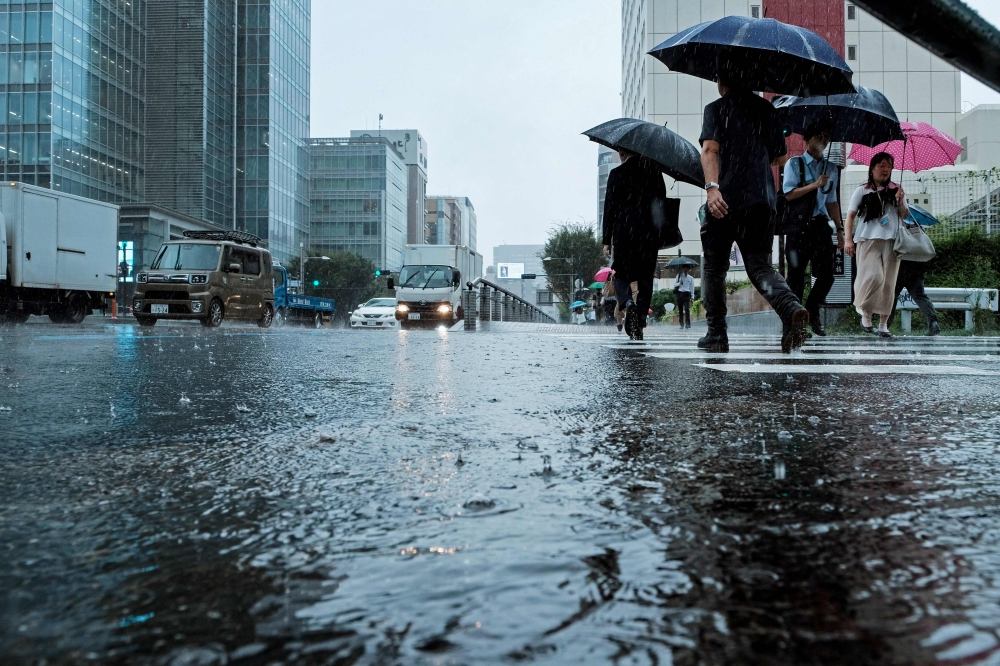 People carrying umbrellas, walk across a street amid heavy rainfall in Tokyo on August 30, 2024. Typhoon Shanshan weakened to a tropical storm on August 30, but was still dumping heavy rains as it slowly churned through Japan, triggering transport havoc and landslide warnings, with up to six people killed. — AFP pic