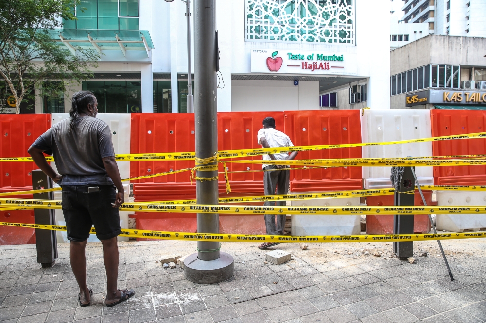 A man crosses the yellow police tape while another watches near a sinkhole at Jalan Masjid India in Kuala Lumpur September 1, 2024. — Picture by Yusof Mat Isa