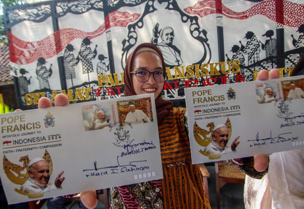 A woman shows samples of a new series of stamps ahead of the visit by Pope Francis during the launch ceremony at the Jakarta Cathedral in Jakarta on September 2, 2024. — AFP pic