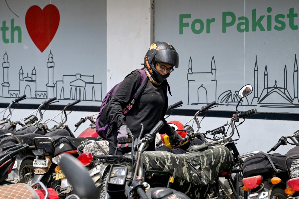 Amina Sohail, a motorbike rider with a local ride-hailing service provider Bykea, parks at their office in Karachi. — AFP pic