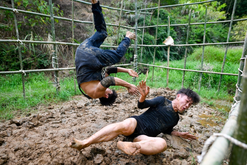 This picture taken on September 12, 2024 shows Wang Tao (right) training with his teammate Chen Wenbin in the mud in the mountain forest in Xingning, in the China southern Guangdong province. When Wang ran away from home at the age of 17 to become a pro wrestler, he knew it would be a hard slog to succeed in China's passionate but underdeveloped scene. — AFP pic