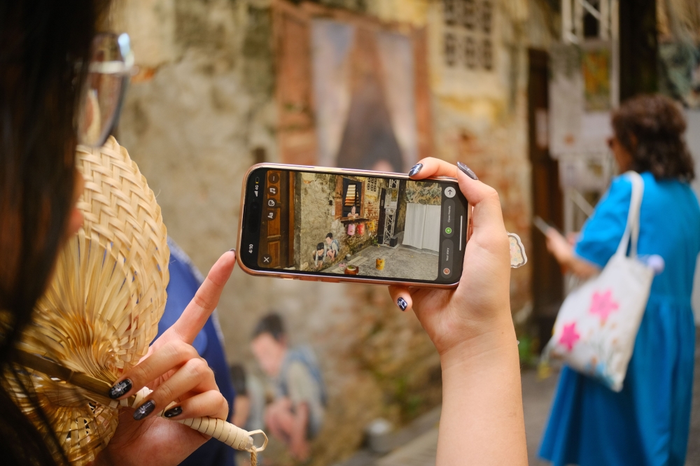 A visitor viewing a mural through AR-activated mode on her mobile phone at Kwai Chai Hong in Petaling Street, Kuala Lumpur. — Picture courtesy of AR Fest KL