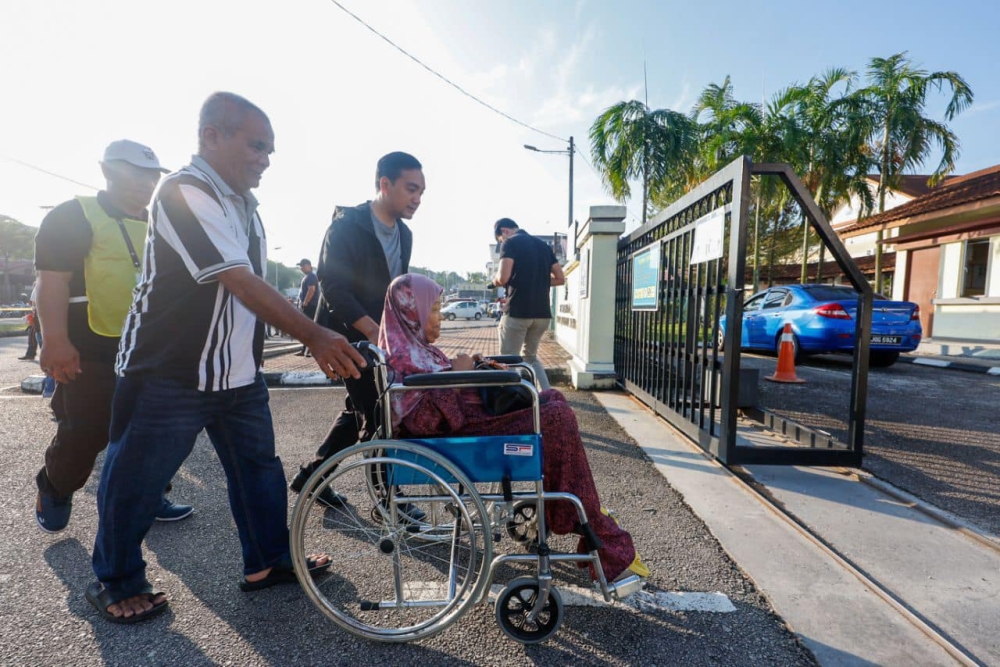 Johor Menteri Besar Datuk Onn Hafiz Ghazi (third from left) escort Mahkota voters Zuriah Saat, 60 (in wheelchair), and her husband Abdul Aziz Osman, 62 (second from left), to their polling station on September 28, 2024. — Picture from Facebook/Onn Hafiz Ghazi 