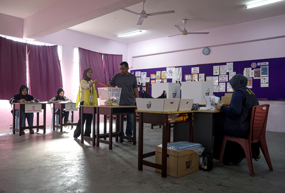 An election officer helps a voter put the ballot paper inside the box at the SMK Seri Perdana polling station for the Mahkota state by-election in Kluang, Johor on September 28, 2024. — Bernama pic