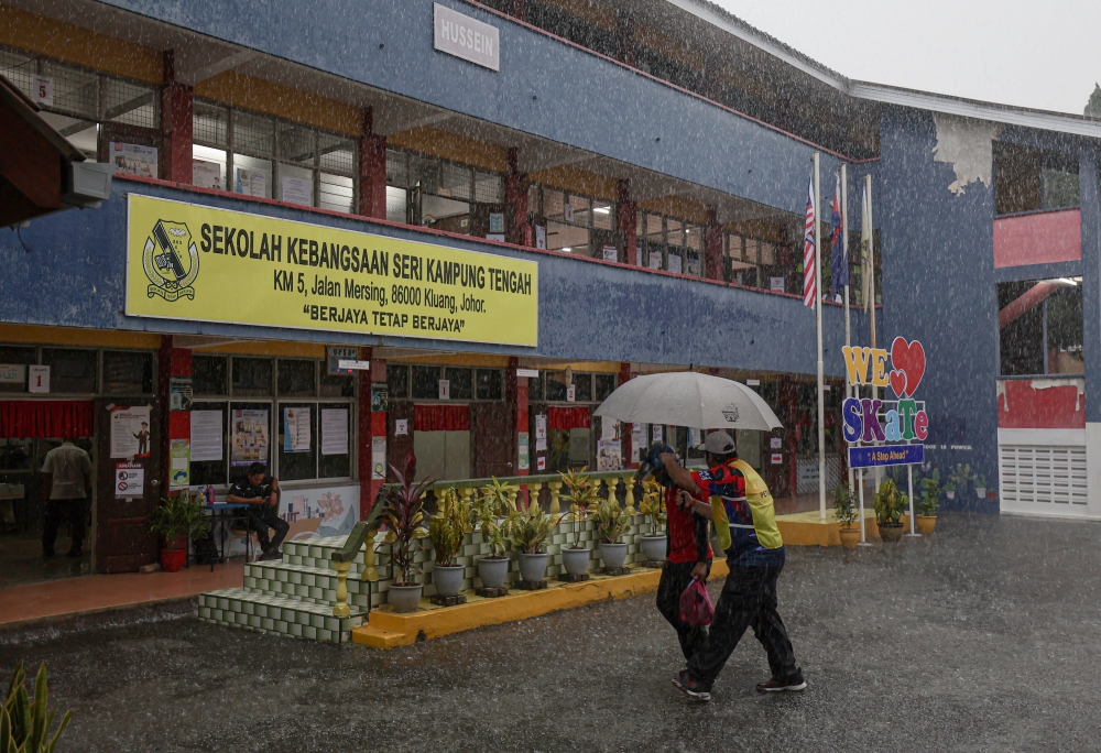 An Election Commission (EC) official assists a voter amid heavy rain during the Mahkota state by-election at Sekolah Kebangsaan Seri Kampung Tengah in Kluang September 28, 2024. — Bernama pic