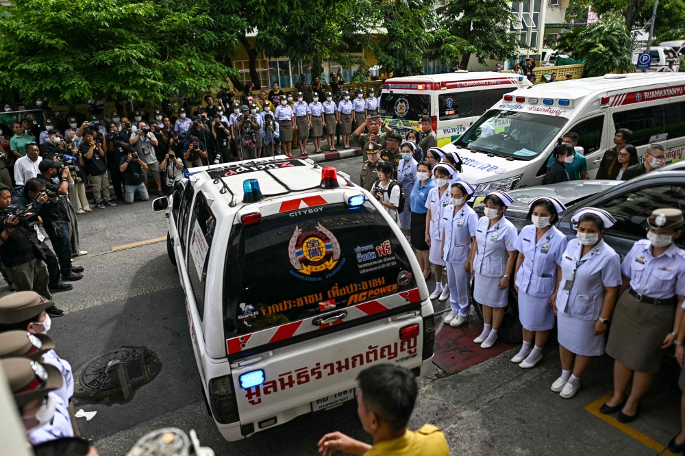 Police officers and nurses stand near media representatives as an ambulance carrying victims' remains leaves the forensic institute at the police hospital in Bangkok, on October 2, 2024. — AFP pic