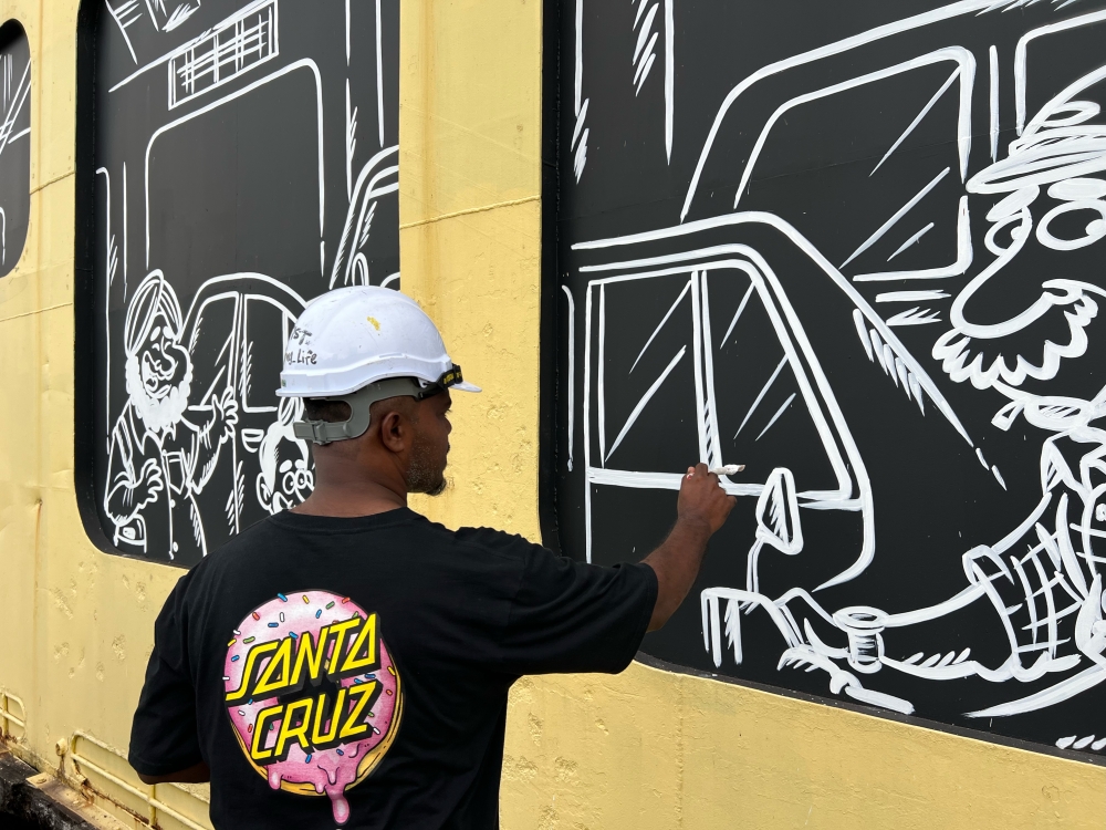 Penang artist Mohd Azmi Mohd Hussin painting his characters as if they are peeking out the “windows” of the ferry. — Picture by Opalyn Mok