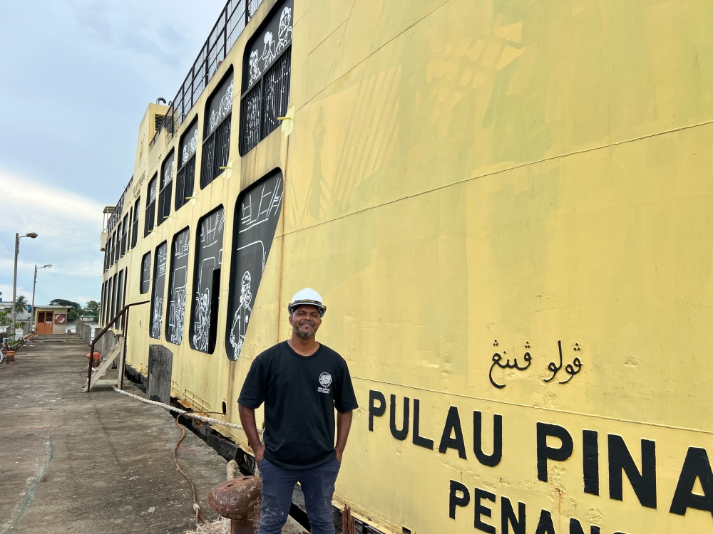 Penang artist Mohd Azmi Mohd Hussin painting his characters as if they are peeking out the “windows” of the ferry that have been blocked up to be turned into the ferry museum. — Picture by Opalyn Mok