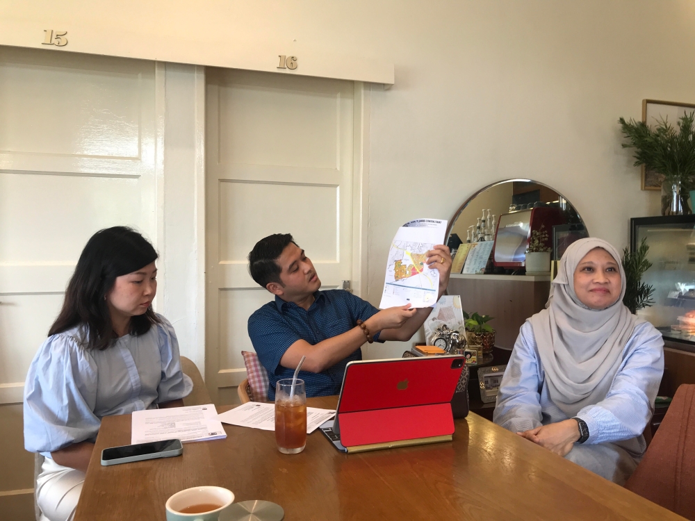 Vincent Perera (centre), his wife Sandra Lee (left) and a friend and patron who declined to be named, show reporters documents that purportedly affirm his land has been changed from residential for commercial purposes during a news conference at the Canning Garden Hillrise Coffee 16 cafe on October 5, 2024. — Picture by John Bunyan