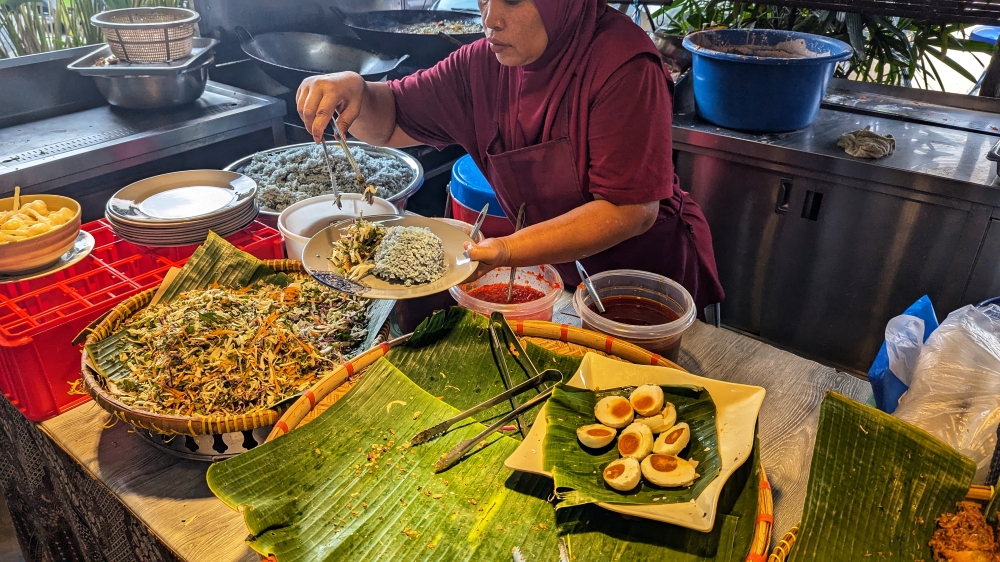 A server dishes out ‘nasi kerabu’ and ‘ulam’ before you add your choice of ‘lauk’. — Picture by Ethan Lau