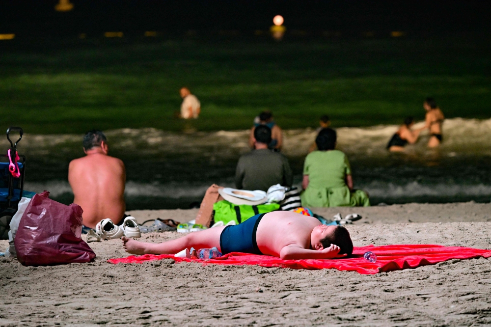 A young boy lies on the sand as others swim at the Umm Suqeim beach in Dubai during the night of October 5, 2024. — AFP pic