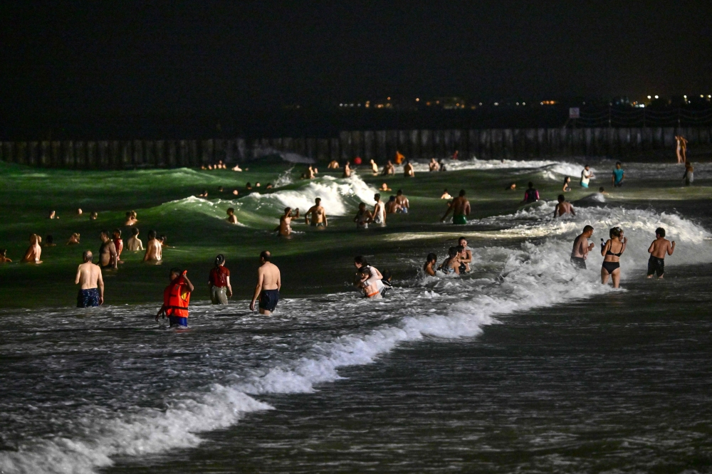 People swim at the Umm Suqeim beach in Dubai during the night of October 5, 2024. — AFP pic