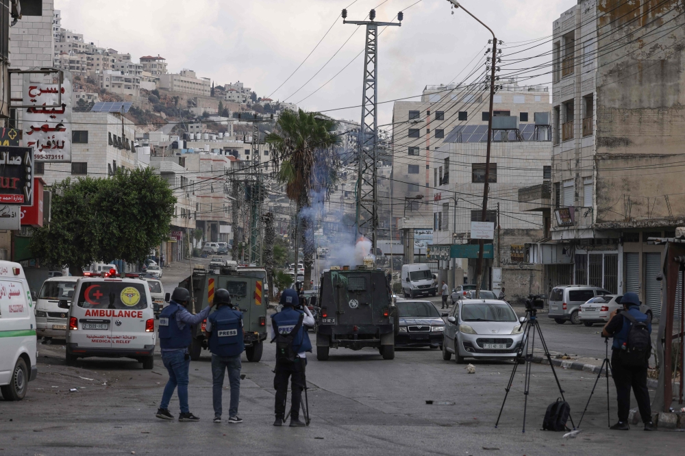 Reporters take images of Israeli military vehicles conducting a raid at the Balata refugee camp, east of Nablus, in the occupied West Bank on October 1, 2024. Italian media, much like its counterparts across Europe, frequently presents a binary narrative when covering Israel. Israel is portrayed as a ‘victim’ of history, deserving sympathy for its role in major historical events such as the Holocaust, writes the author. — AFP pic 