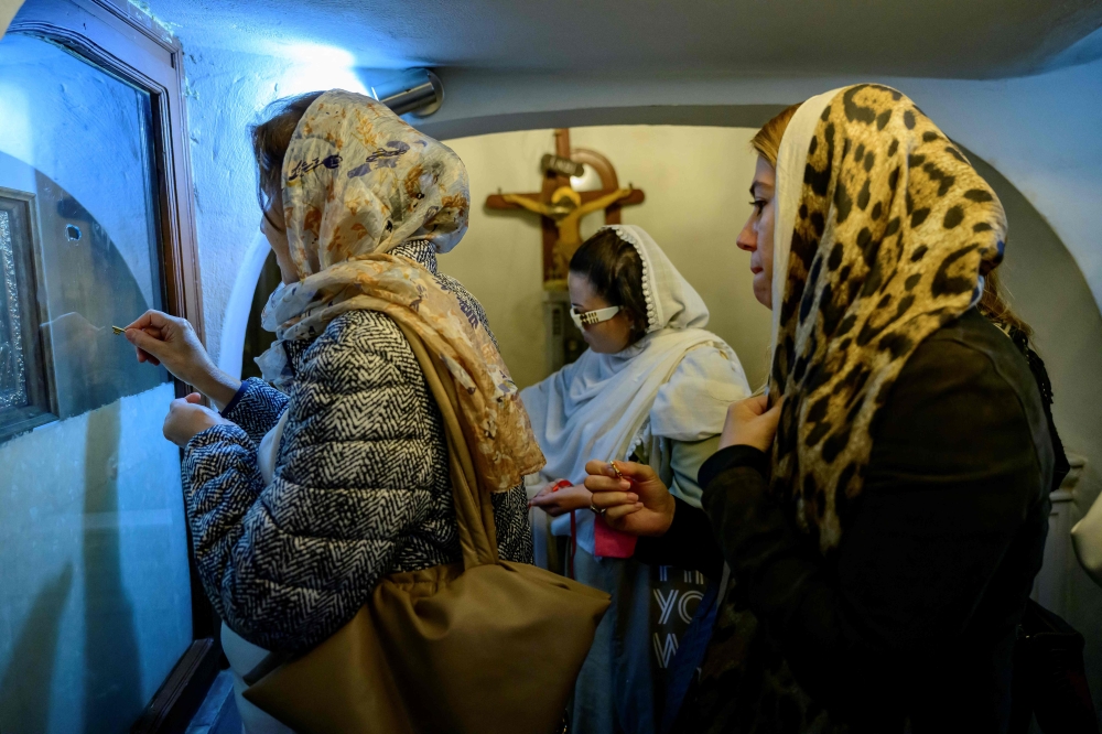 Women rub the keys they bought in church on the glass portraits to make wishes at the Our Lady of Vefa church in Istanbul, on October 1, 2024. — AFP pic