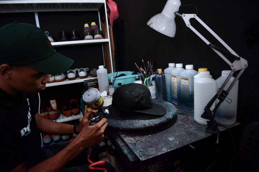 Firm Bundle employee, Muhammad Alif Idham Abdull Rashid, 23, applies colour on a customer’s hat at Firm Bundle Boutique recently. — Bernama pic