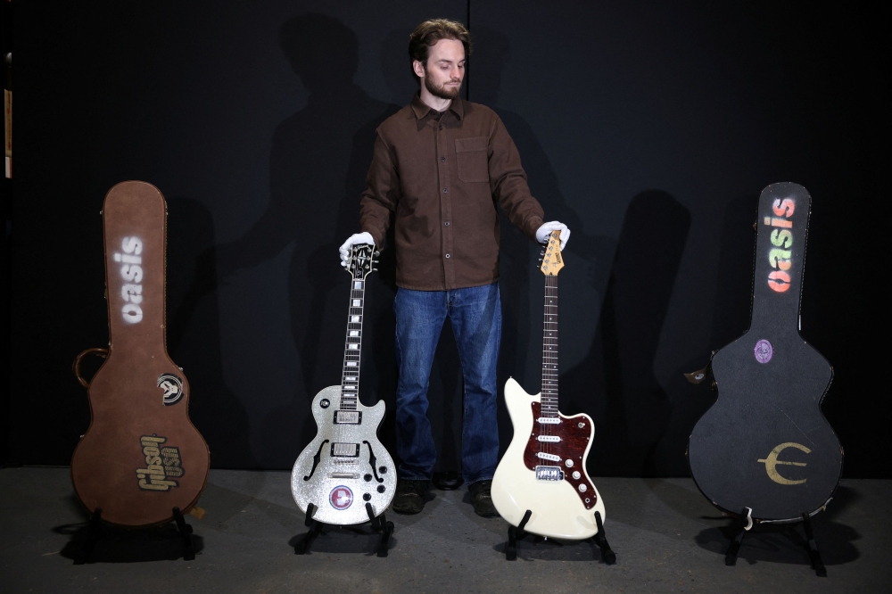 An employee poses with Noel Gallagher's Custom Silver Sparkle Gibson Les Paul Florentine guitar and Cream Hohner JT60 guitar at Propstore in Chenies September 30, 2024. — Reuters pic  