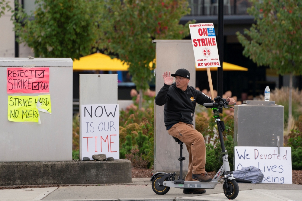 A person holds a strike sign while riding a scooter as Boeing factory workers and supporters gather on a picket line near the entrance to a Boeing production facility in Renton, Washington October 11, 2024. — Reuters pic  