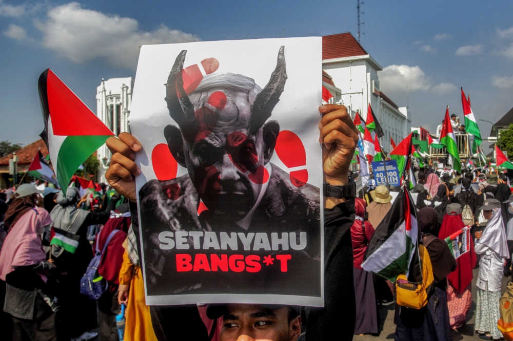 A pro-Palestinian protester holds a poster depicting Israeli Prime Minister Benjamin Netanyahu as a devil reading 