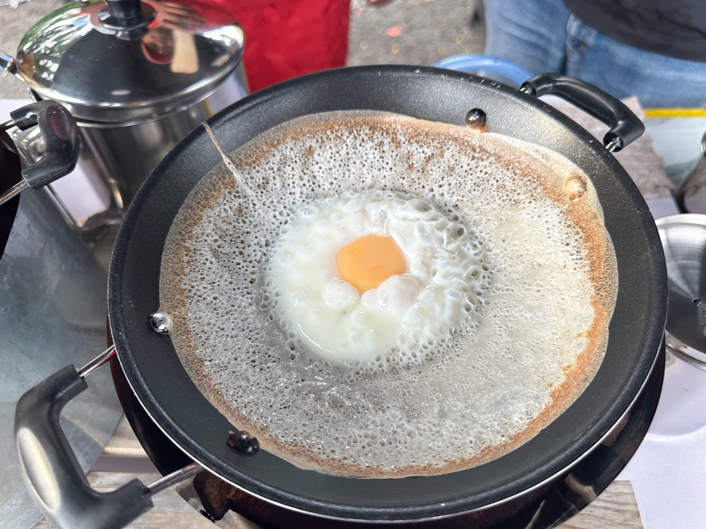 There are two types of egg 'apom manis', one with an egg cracked in the middle or another where the egg is completely mixed into the batter to give it a richer taste. — Picture by Lee Khang Yi