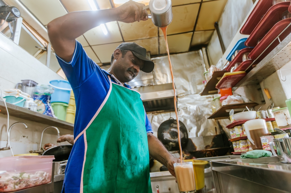 Drinks stall vendor Gopinand, 47, pulls tea to create a froth at his stall in Putrajaya on March 7, 2024. — Picture by Raymond Manuel