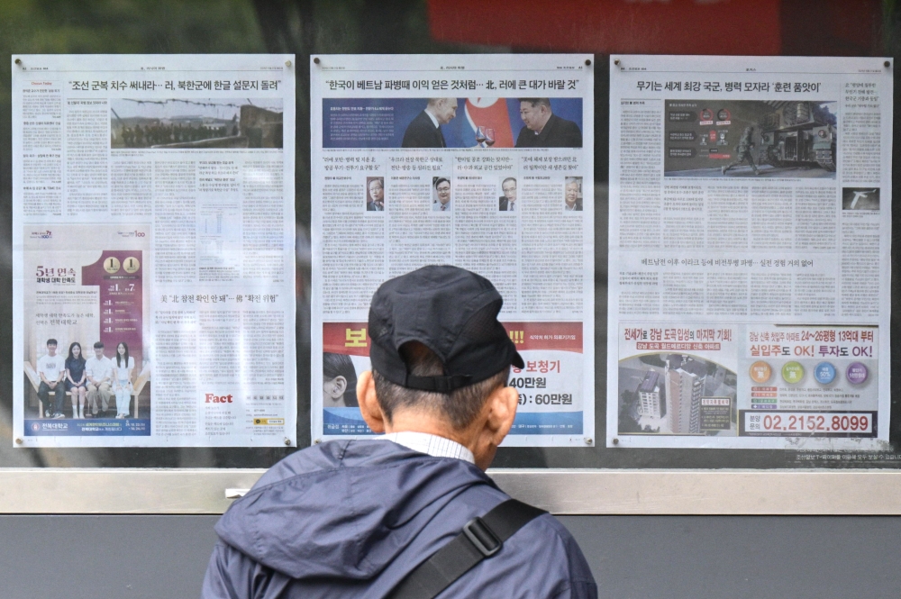 A man walks past a newspaper displayed on a street for the public in Seoul on October 21, 2024, with coverage on North Korea’s decision to deploy thousands of soldiers to Ukraine’s front lines and a photo (centre) of North Korean leader Kim Jong-un and Russia’s President Vladimir Putin toasting at a banquet in Pyongyang earlier this year. — AFP pic