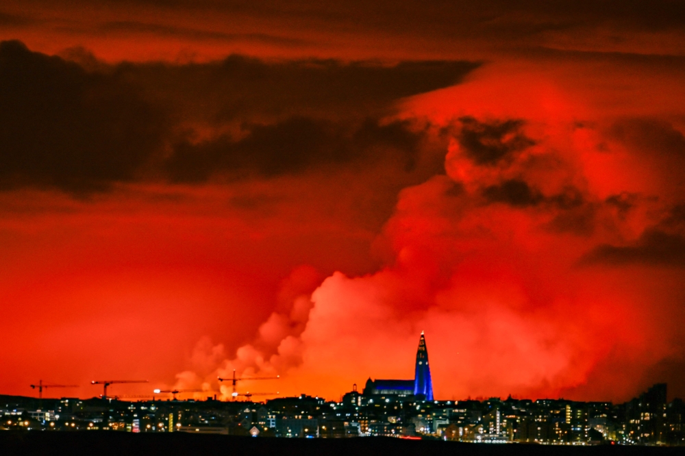 The skyline of Reykjavik is against the backdrop of orange coloured sky due to molten lava flowing out from a fissure on the Reykjanes peninsula north of the evacuated town of Grindavik, western Iceland on March 16, 2024. — AFP pic