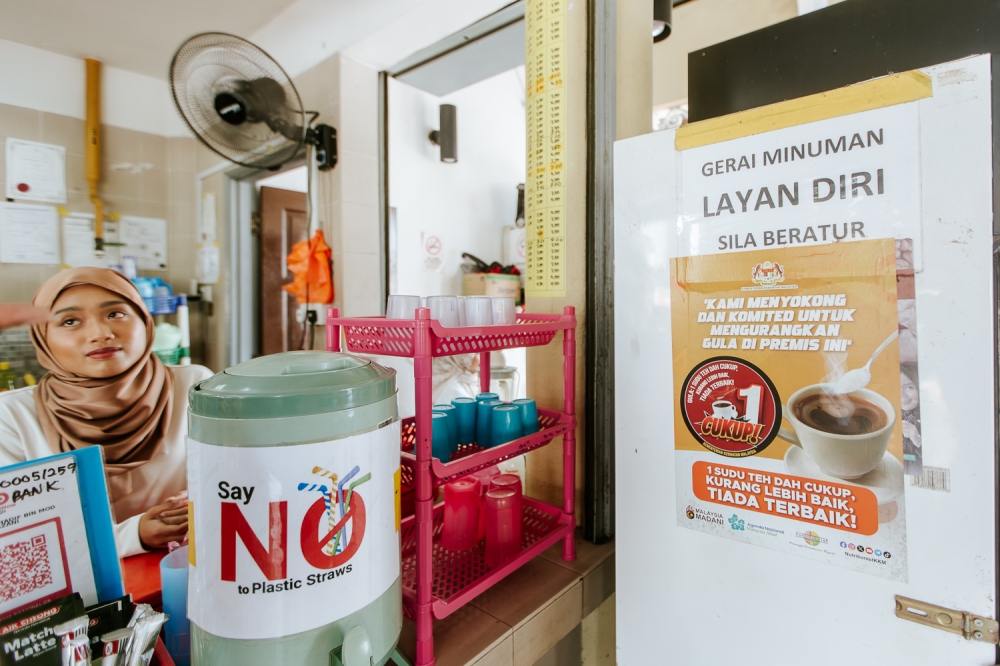 A poster promoting sugar reduction in beverages is displayed at a coffee shop in Putrajaya on March 07, 2024 — Photo by Raymond Manuel