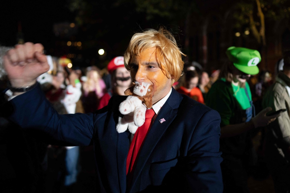 A person dressed as Donald Trump holds a stuffed toy in his mouth during the 51st Annual Halloween Parade in lower Manhattan, New York, October 31, 2024. — AFP pic