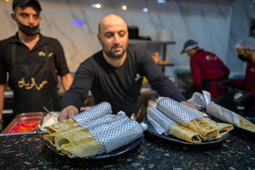 A waiter serves Gaza-style turkey shawarma sandwiches, wrapped in paper with the Kefiyeh pattern. — AFP pic