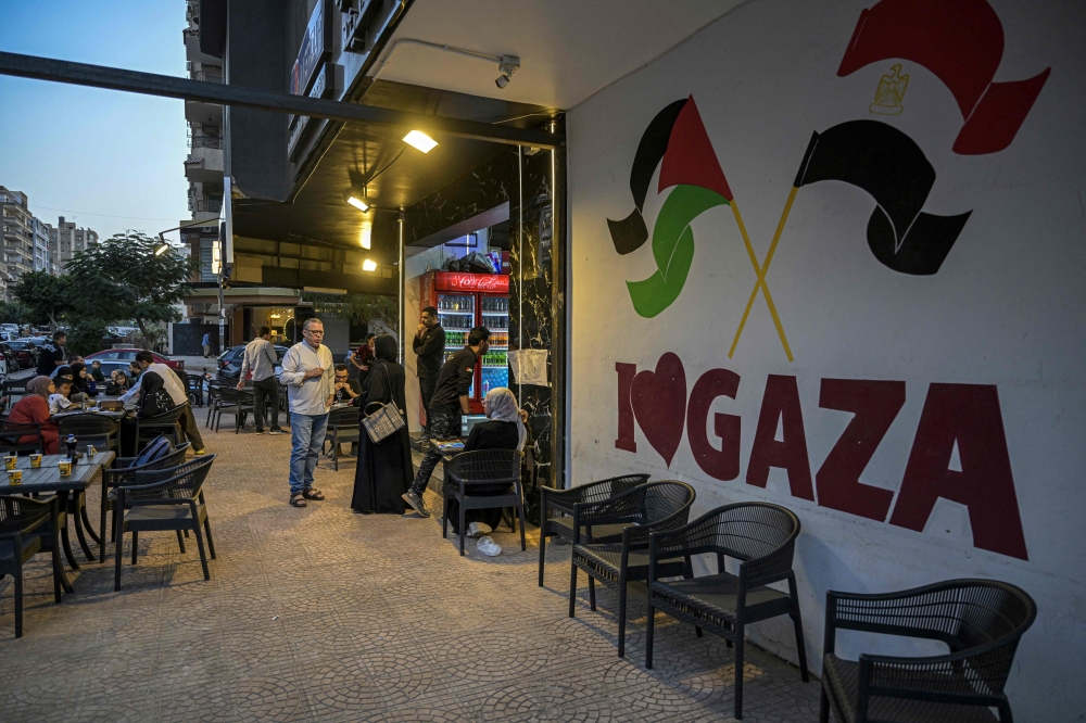 Palestinian restaurant-owner Bassem Abu Aoun speaks to a customer in front of establishment ‘Hay Al-Rimal’, named after his neighbourhood in Gaza City, in Cairo on October 28, 2024. — AFP pic