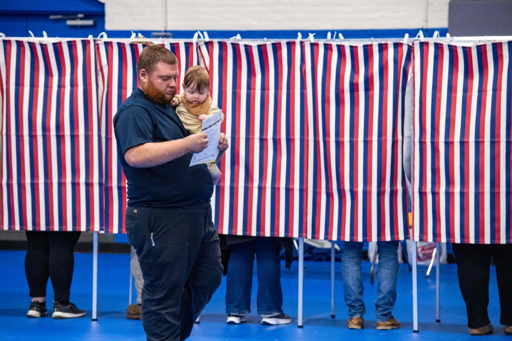 A person carries a baby with a filled out ballot after voting at the Green Street Community Center in Concord, New Hampshire, on November 5, 2024. — AFP pic