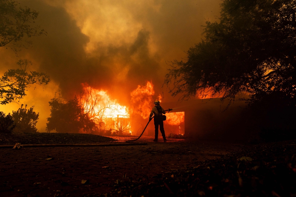 A firefighter tries to control the fire burning down a house as the Mountain Fire scorches acres, the wildfire fueled by strong Santa Ana winds, in Camarillo, California November 6, 2024. — AFP pic