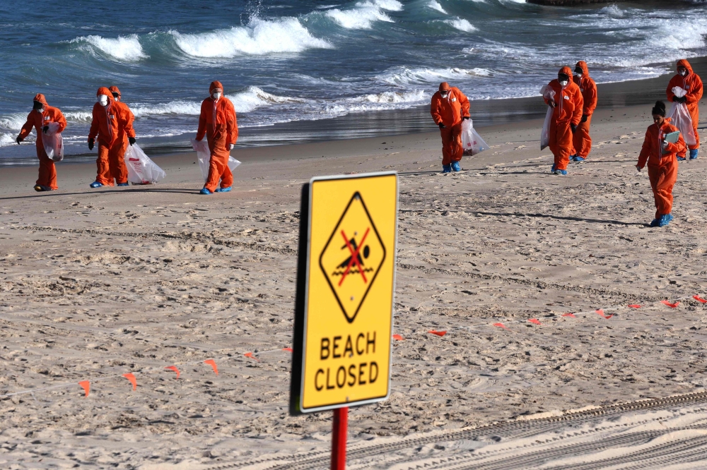 Workers in protective suits conduct a cleanup operation to clear the mystery black balls ranging from the size of peas to tennis balls that washed ashore on Coogee Beach in Sydney that were initially feared to contain toxic substances on October 17, 2024. — AFP pic