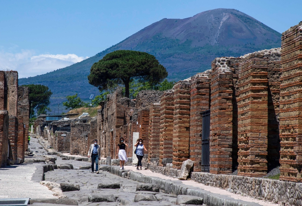 Visitors walk across the archeological site of Pompeii at the bottom of the Mount Vesuvius volcano (rear) on May 26, 2020. — AFP pic