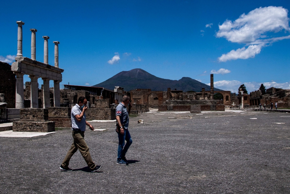 People walk across the archeological site of Pompeii at the bottom of Mount Vesuvius volcano (rear) on May 26, 2020. — AFP pic