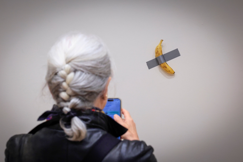 A woman takes a picture of Italian visual artist Maurizio Cattelan’s duct-taped banana titled “Comedian,” displayed during a media preview at Sotheby’s in New York, on November 8, 2024. — AFP pic